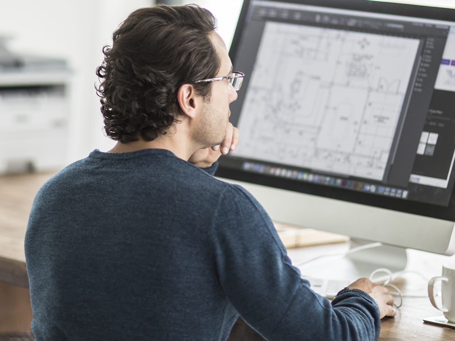 A man printing a document from an all-in-one computer while sitting at a desk in a home office environment