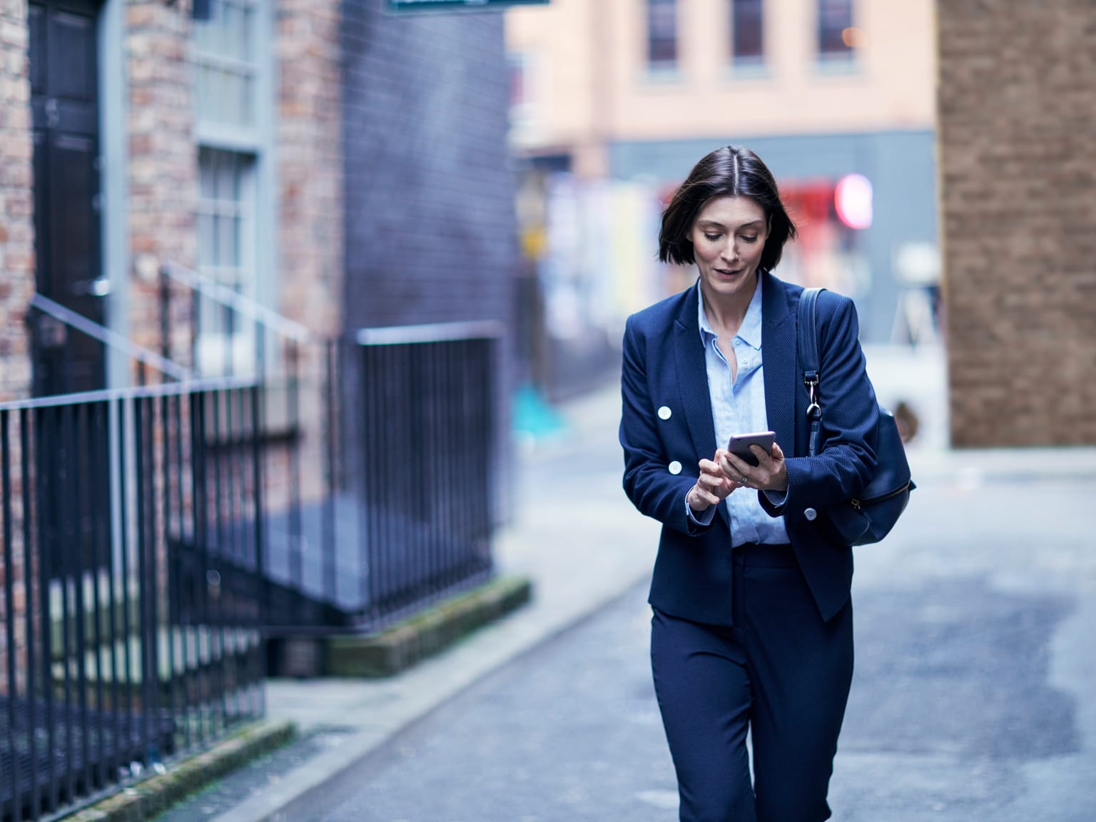 A woman looking at her smartphone while walking down a street