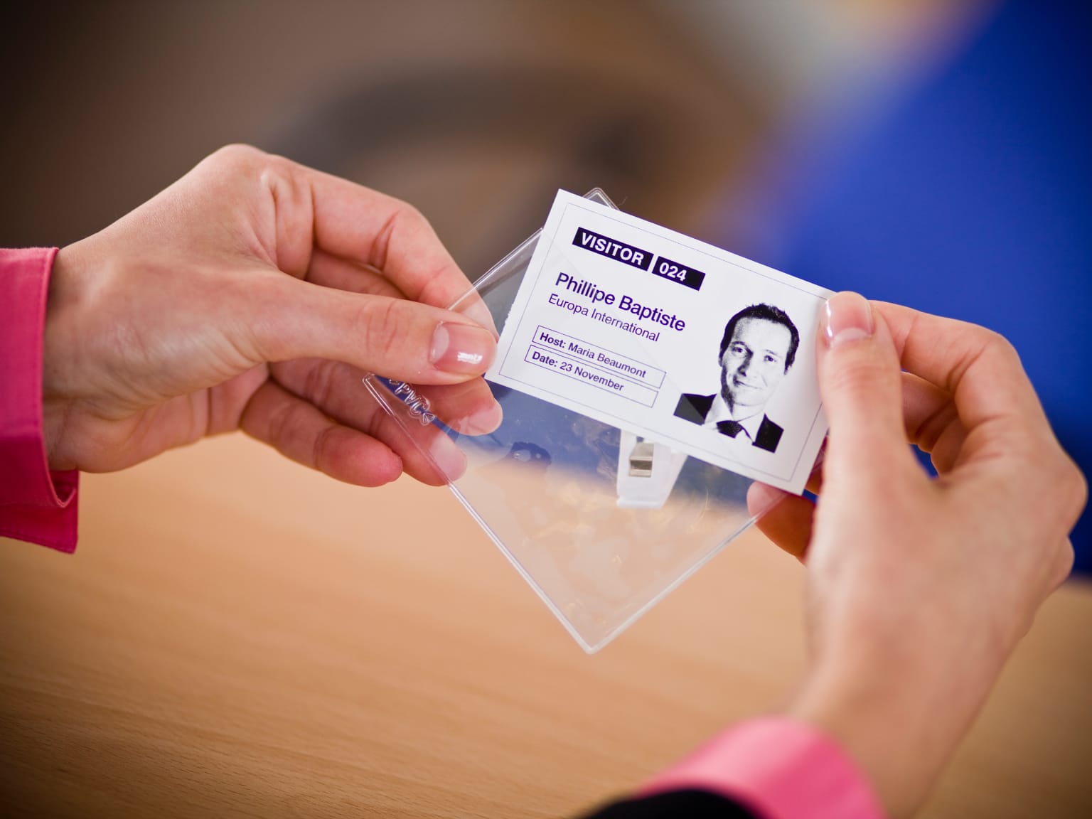 Close-up of a woman inserting a visitor ID printout into a clear clip-on badge