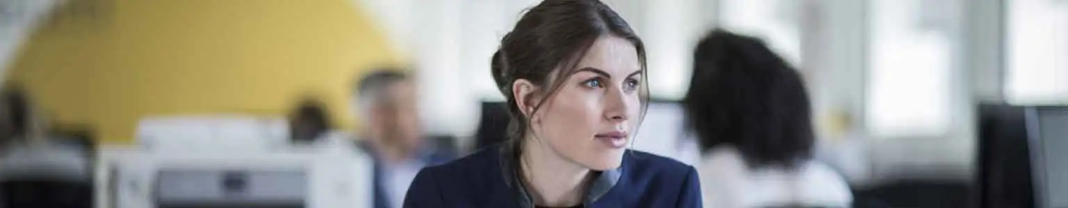 A woman working in an office on her laptop sits at a desk with a Brother business printer in the background