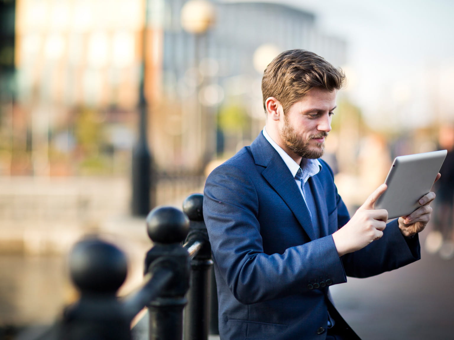 Businessman using table device while leaning against bridge handrail