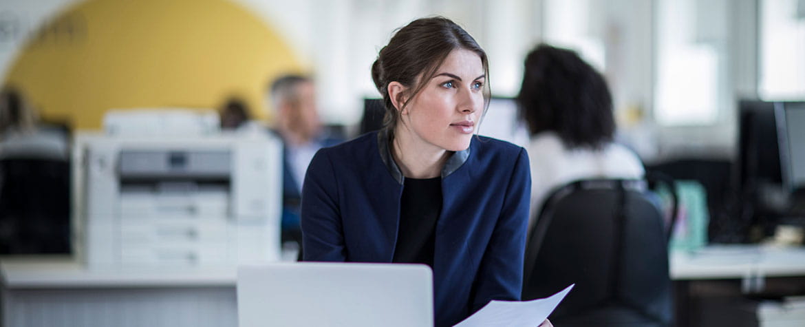 Woman in office sits at desk with print out from Brother printer in her hand