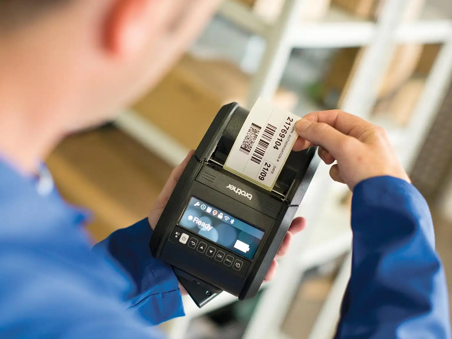 A warehouse worker holds an RJ series label printer in their hand whilst a label is being printed