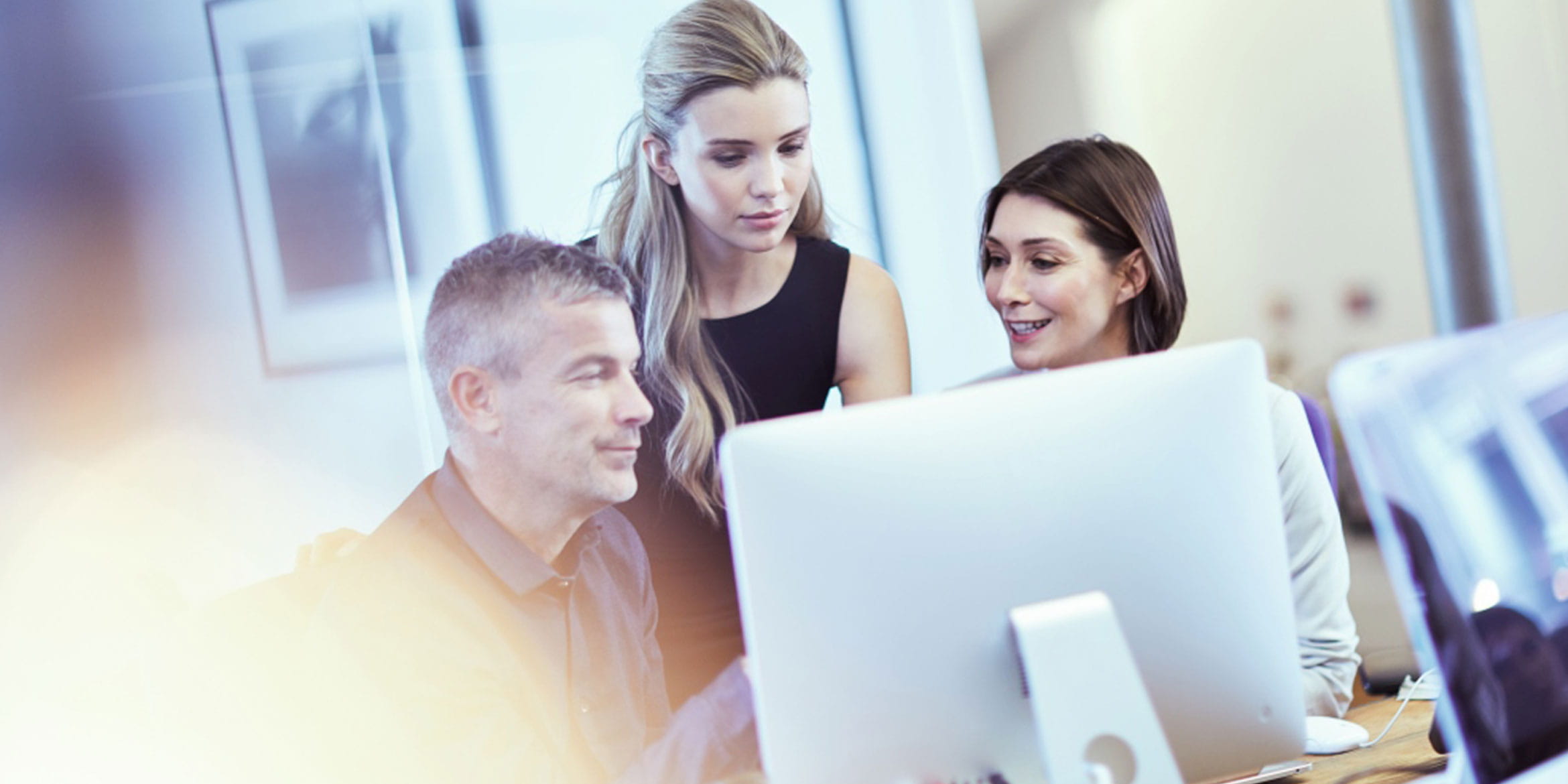 Three colleagues looking at a computer monitor in an office environment