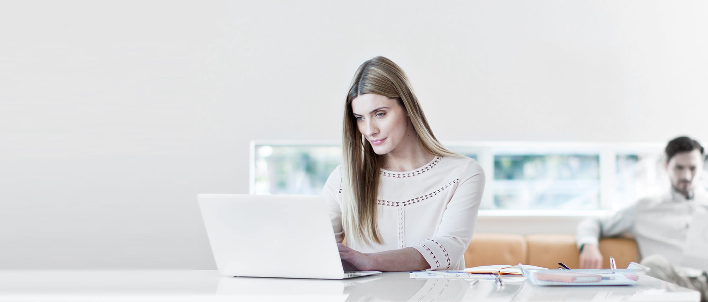 Frau in Büro Ein Laptop Sitzend, Mann auf Couch im Büro im Hintergrund