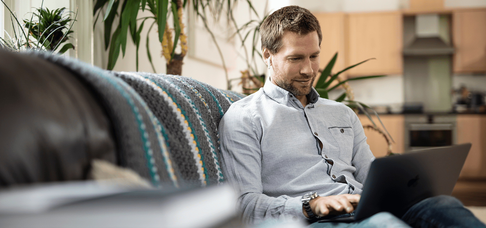 Mann, der von zu Hause aus Arbeitet, auf Sofa sitzend mit Laptop