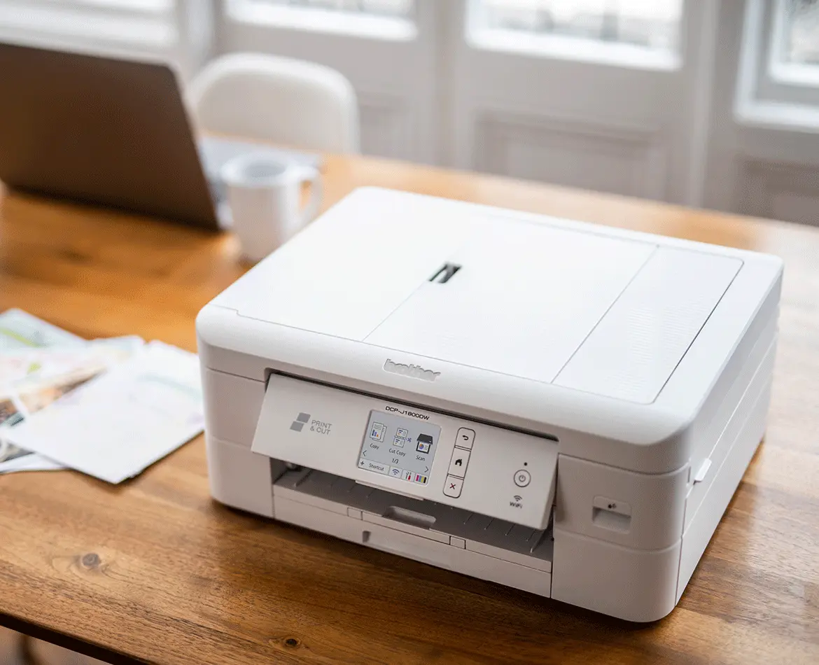 Multifunktionsdrucker DCP-J1800W von Brother auf einem Tisch. Ein Laptop steht im Hintergrund.