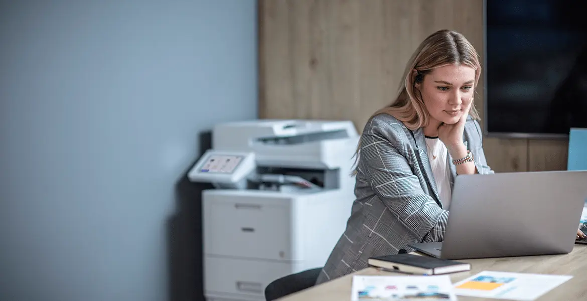 Eine Frau sitzt im Büro am Laptop, Brother Laserdrucker im Hintergrund