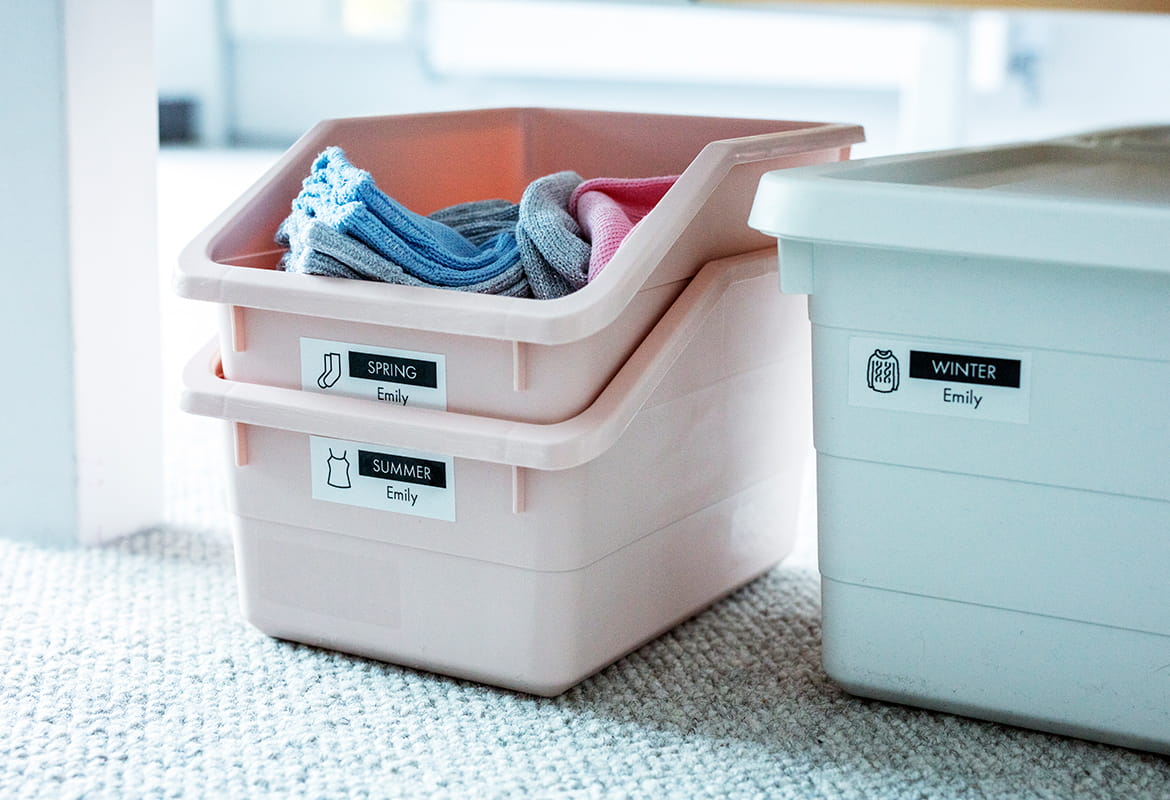 Two pink and one blue box filled with clothes placed under a bed