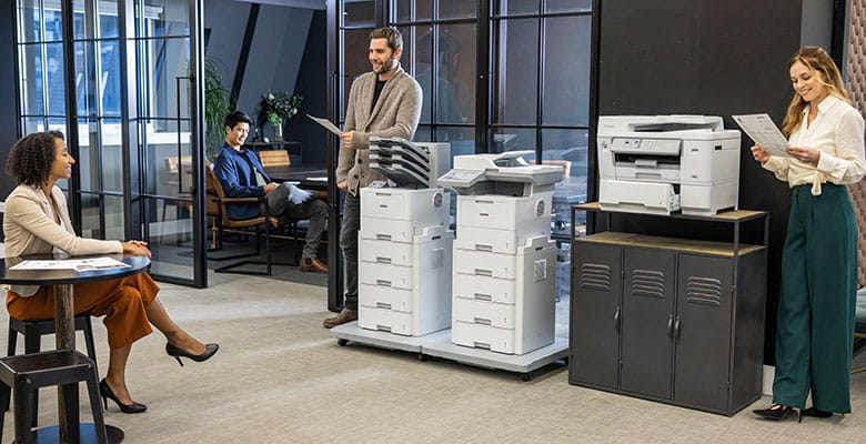 Large, busy office with row of Brother printers. 2 men, 2 women, cabinet, desks, chairs