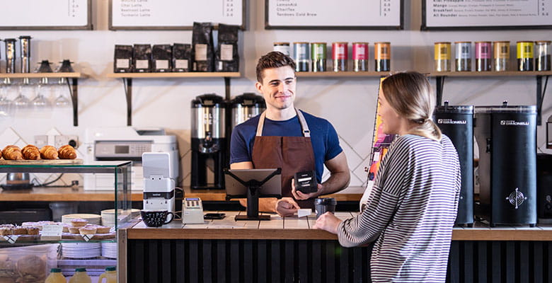 Male barista in coffee shop serving female customer