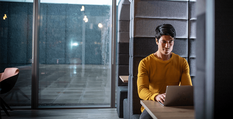 A man using a laptop computer while sat in a booth in an office environment