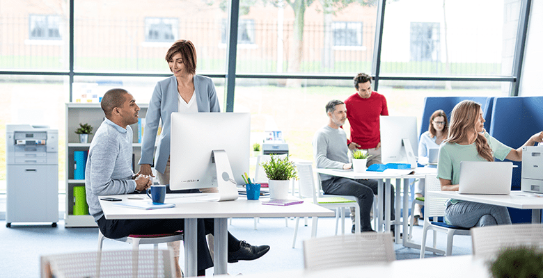 Male and female colleagues talking at a desk in a busy office environment