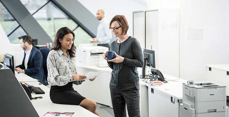 Two female colleagues having a discussion in a busy office environment