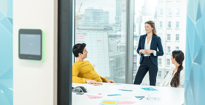 Three colleagues in an office meeting room with floor to ceiling windows behind them