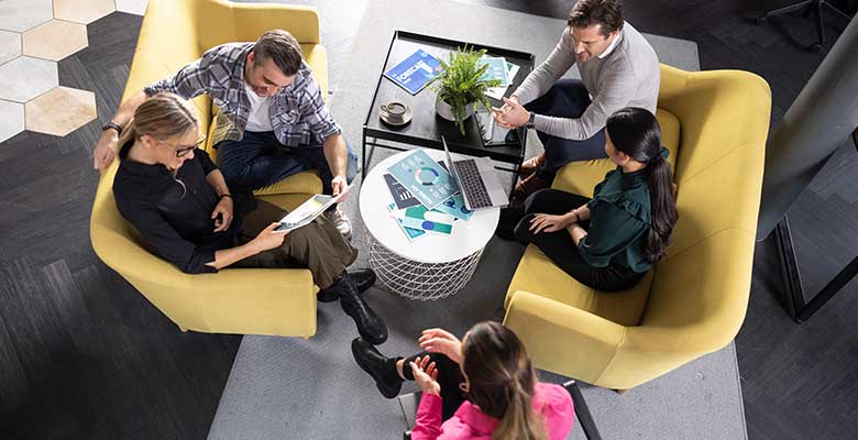 Group of people sat on sofa and chairs around table with colour documents